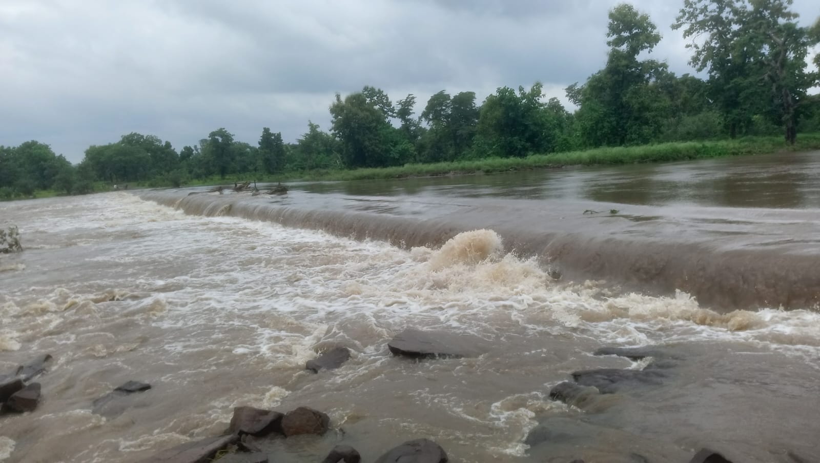 Monsoon water spilling over a low weir in the river