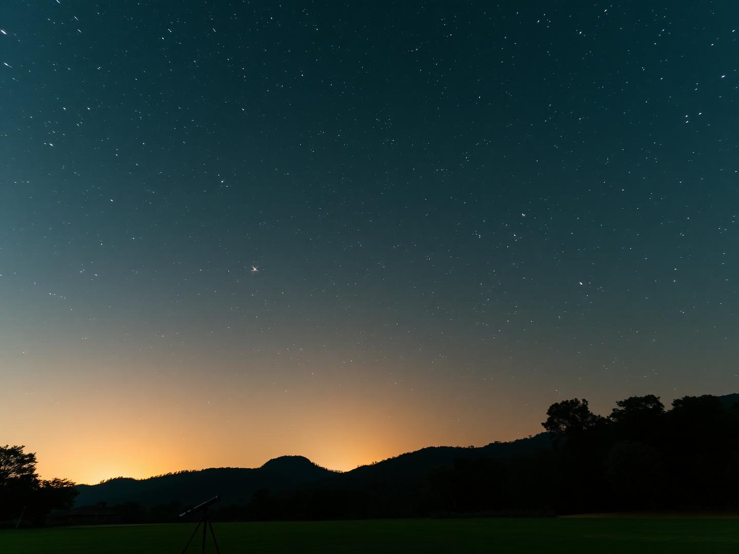 Star filled night sky above silhouetted forest hills with a telescope on the lawn